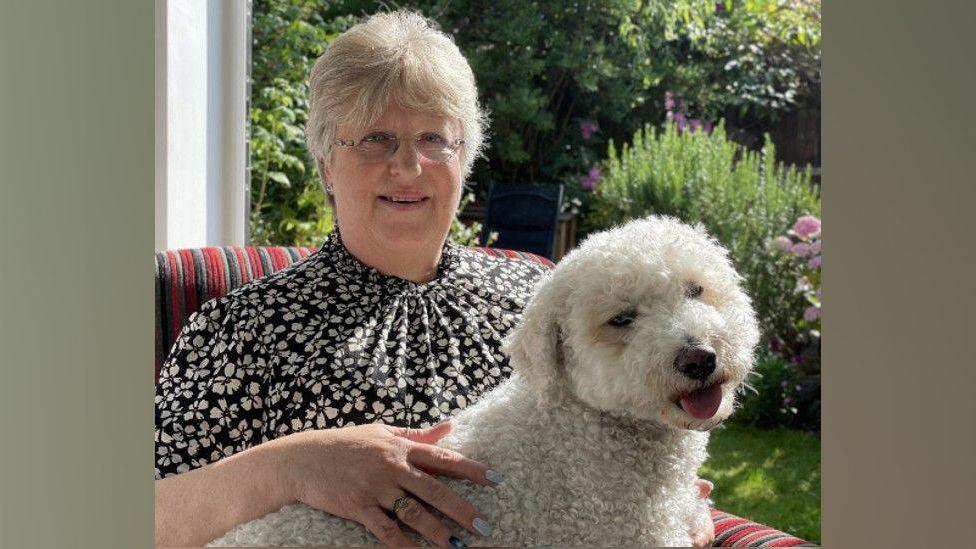 Gail Ward with her dog on her lap, sitting by a doorway to the garden