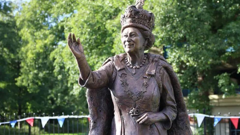 Close up of bronze statue of Queen Elizabeth II smiling and waving while wearing crown and royal robes