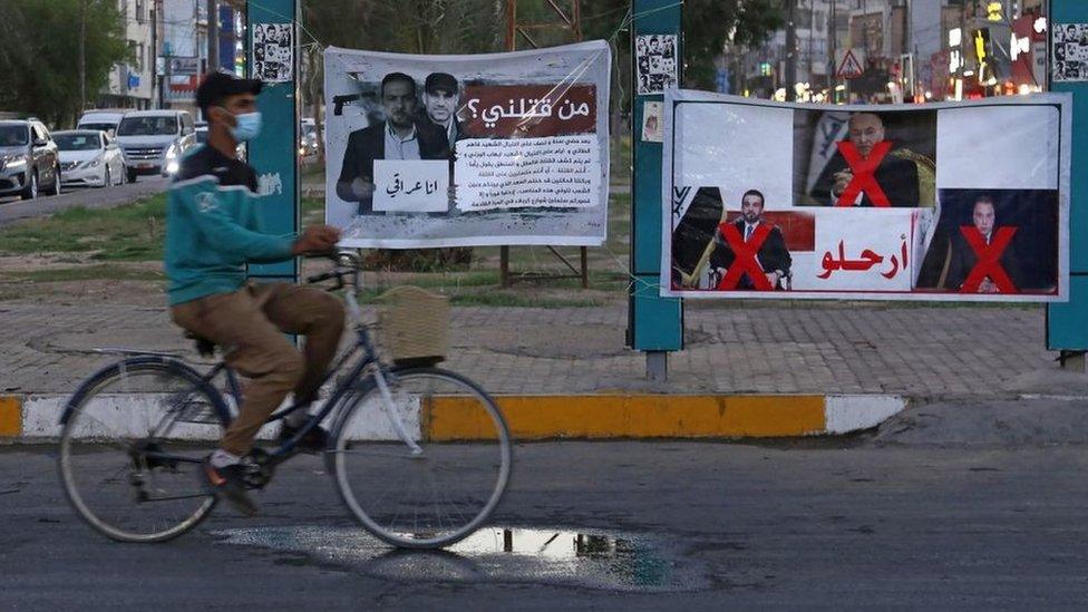 A man rides his bicycle past a banner in Karbala reading in Arabic "Who killed me?" and depicting renowned Iraqi anti-government activist Ehab al-Wazni, who was shot dead (23 May 2021)