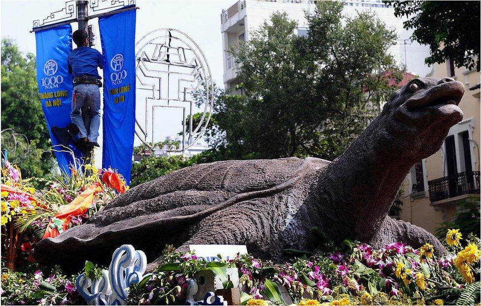 A worker installs banners marking the millennium anniversary of Hanoi next to a model of the capital's Hoan Kiem lake legendary turtle on display in the centre of Hanoi on 30 September 2010