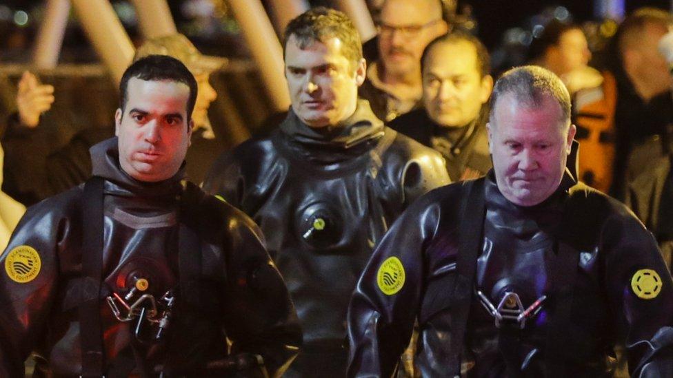 Emergency services divers look downcast as they walk by the waterside