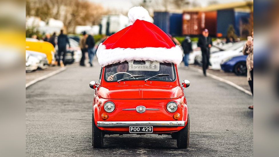 A red Fiat car with a giant santa hat on the top