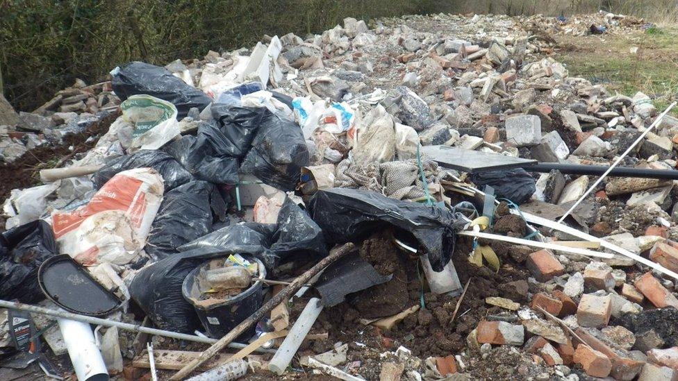 A large pile of rubble mixed with rubbish, like black plastic bin bags