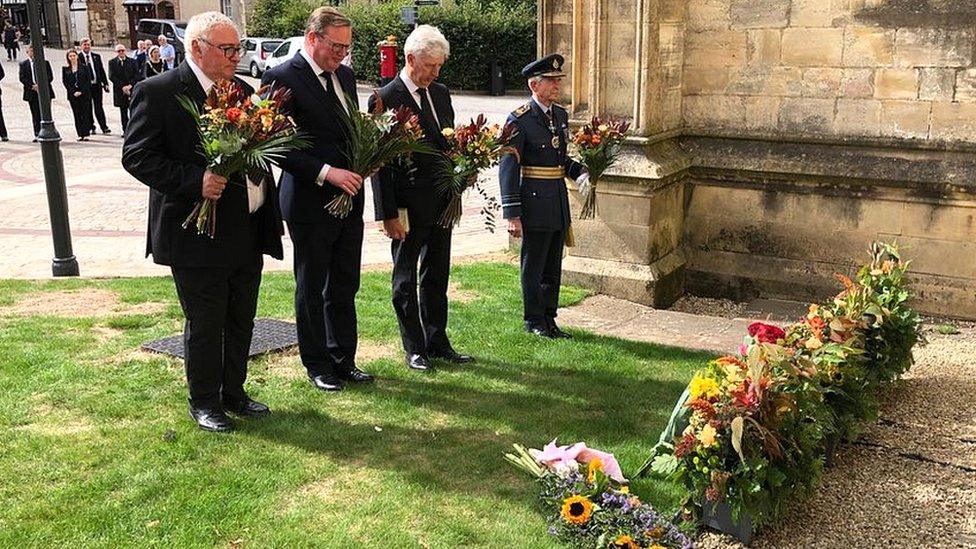 Cllr Alan Preest, Chair of Gloucesterhire County Council, Cllr Mark Hawthorne, leader of GCC, Edward Gillespie, Lord Lieutenant and Sir Dusty Miller, High Sheriff of Gloucestershire lay what would have been the winners flowers from the Tour of Britain outside Gliucester cathedral in memory HRH The Queen.