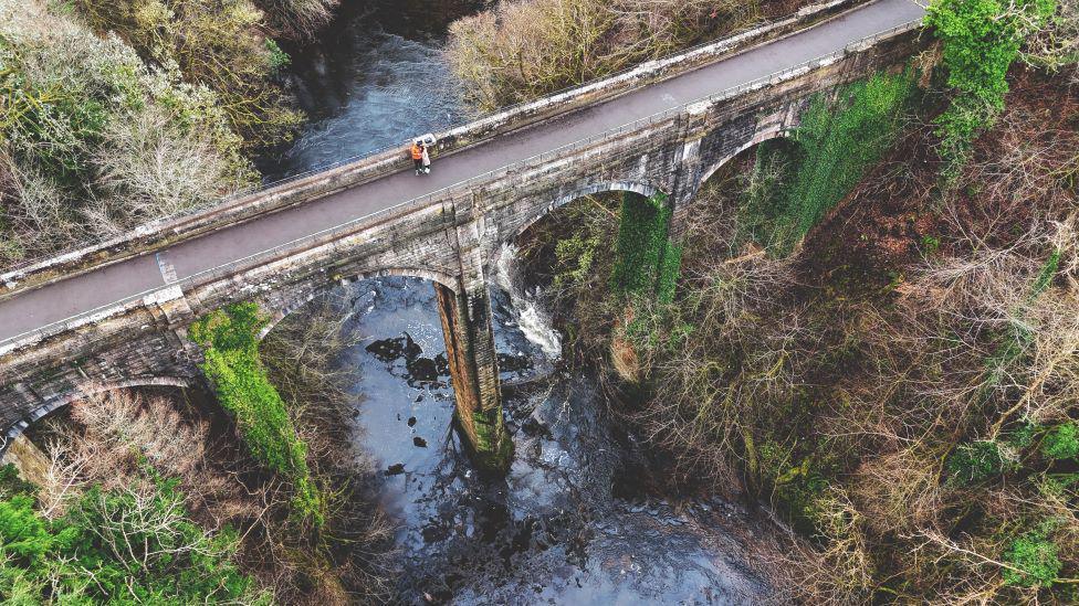 Aerial view of a tall bridge over a river. The bridge is made up of arches and pillars.