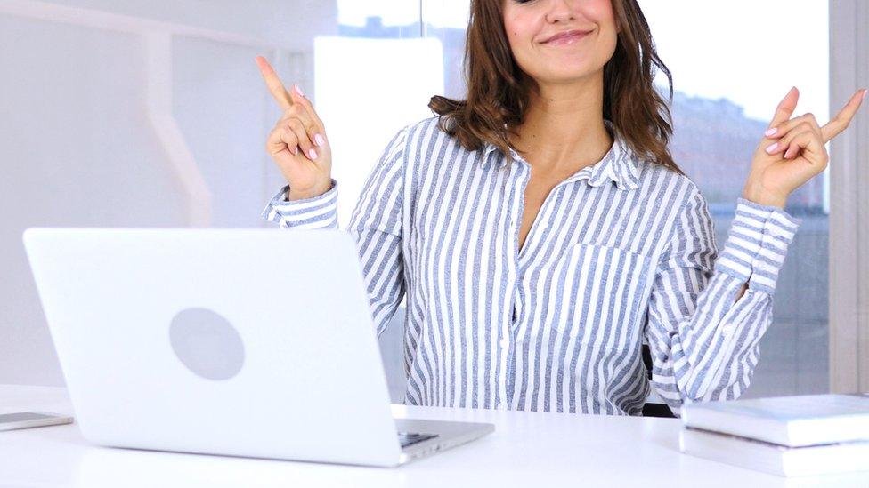 A stock image of a woman smiling and dancing in front of her computer