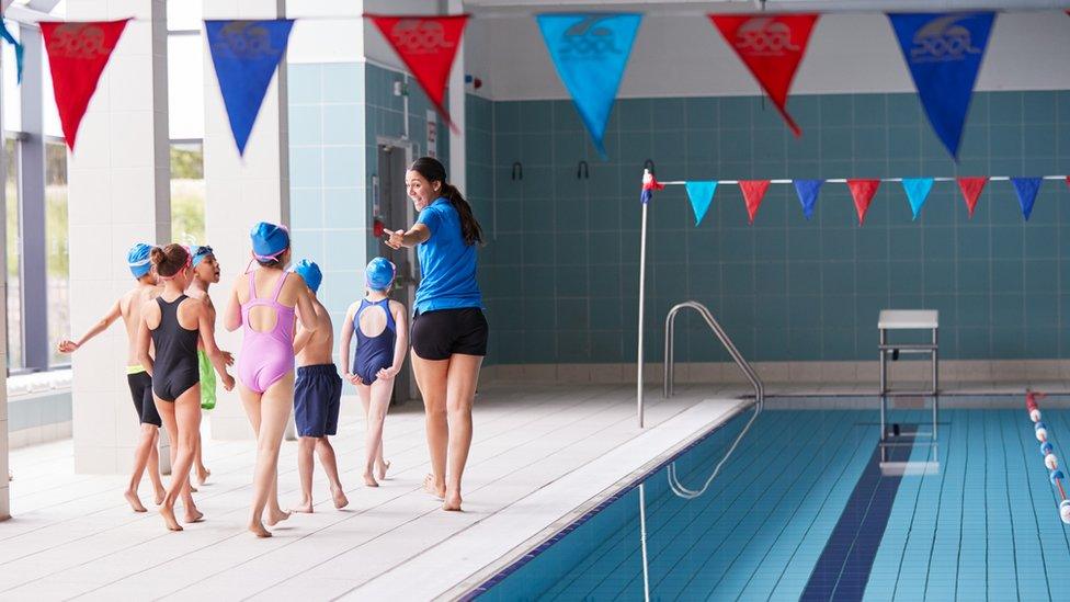 kids-walking-beside-swimming-pool-with-teacher