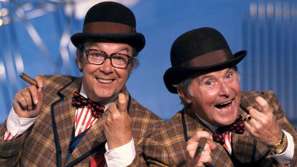 Comedians Eric Morecambe and Ernie Wise dressed in checked suits, bowler hats and holding cigars during a rehearsal for their series The Morecambe & Wise Show, circa 1981