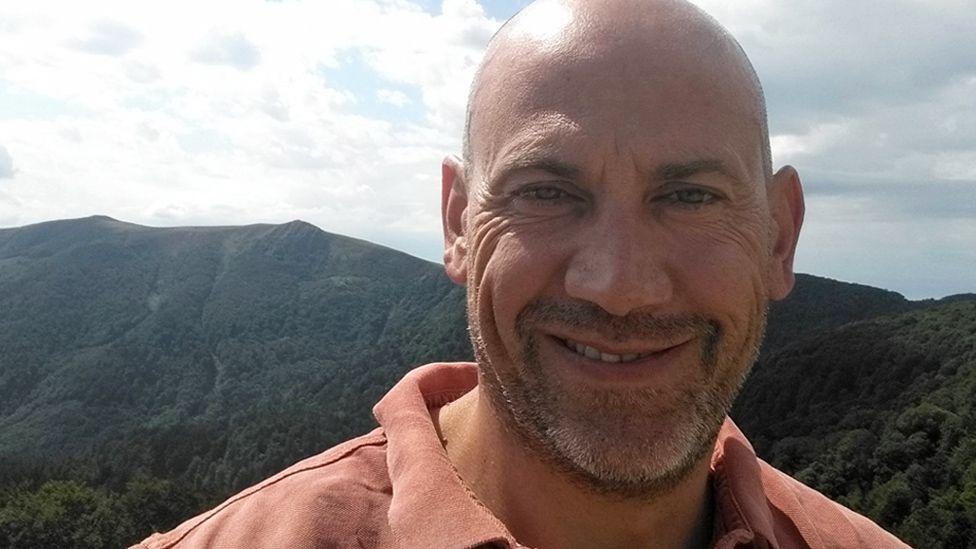 Head shot of Claude Wehrle with a mountainous region behind him. 