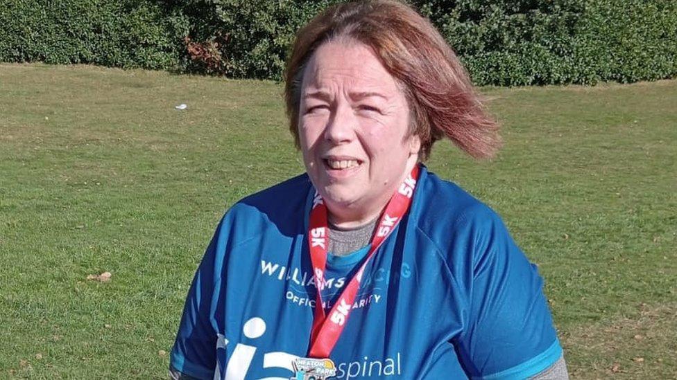 A woman with red hair with a medal around her neck and wearing a blue shirt stands in a field.