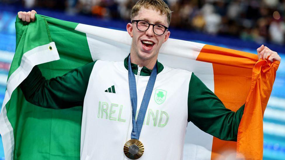 Daniel Wiffen poses with an Irish flag around his shoulders and his olympic gold medal hanging around his neck