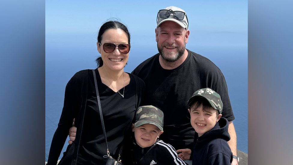 A family photo with ben, his brother, his mum and his dad Alex. They are stood in front of an ocean.