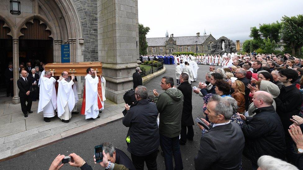 Dr Daly's coffin is carried from the church as mourners look on