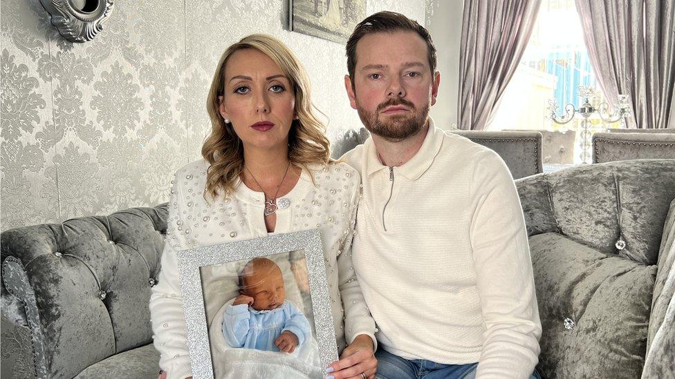 Joann and Christian in their lounge holding a photo of Elijah