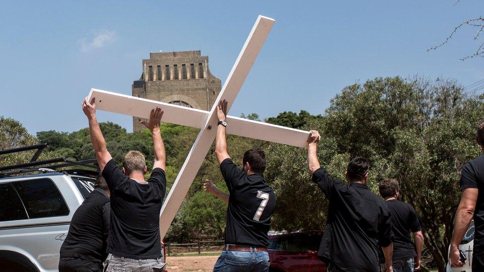 White South African activists haul a white cross aloft from the back of a jeep - to protest a rise in farm murders in the country.