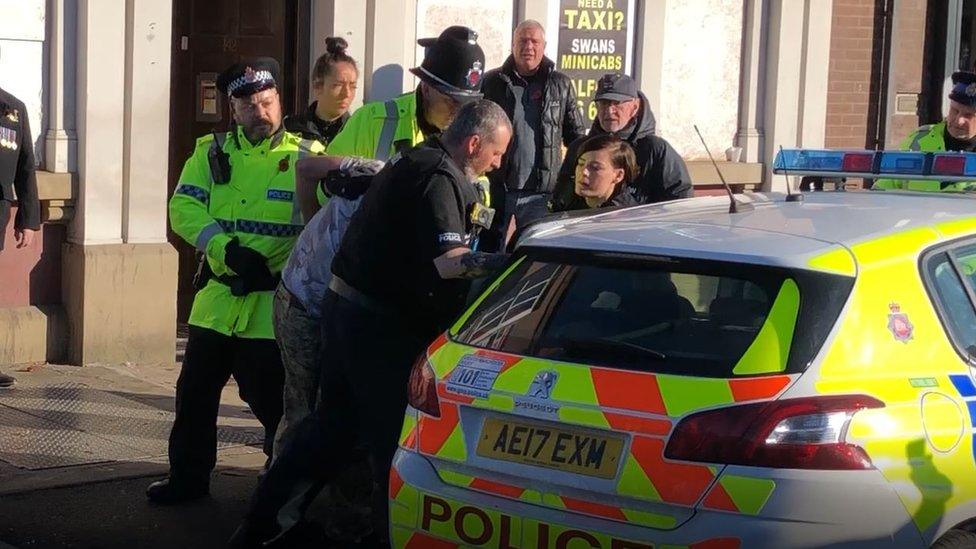 A man is bundled away by police to protect him from an angry crowd after he disrupted a silent tribute with fireworks at a Remembrance Sunday event at the cenotaph in Eccles