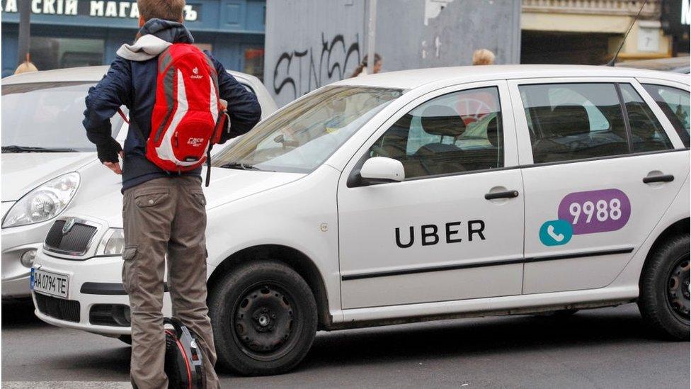 :A man seen on an electric unicycle at a crosswalk in front of a white car with a logo of Uber taxi cab company in Kiev, Ukraine