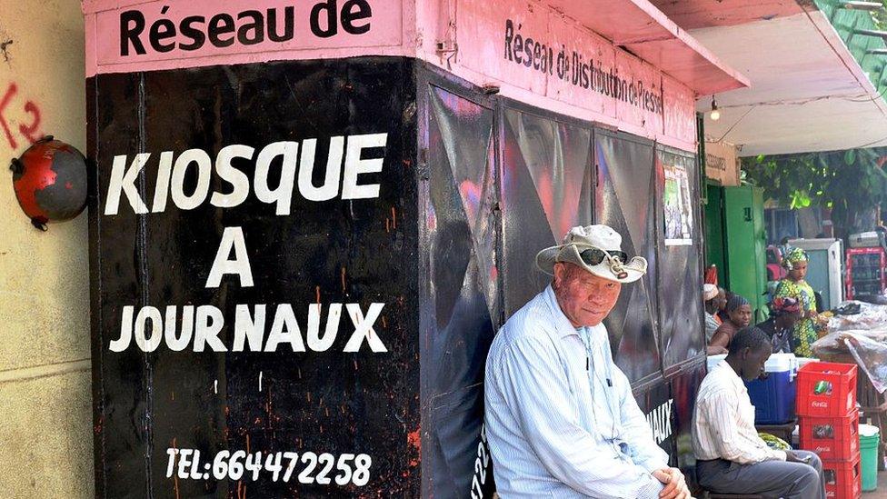 Men sit in front of a closed newspaper stand in Conakry on February 9, 2016, on a "press-free day" in honour of a journalist who was shot dead