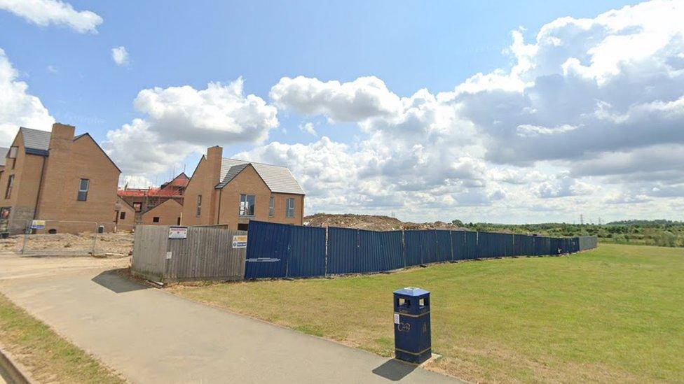 Large open grass area separated from houses under construction by a blue fence