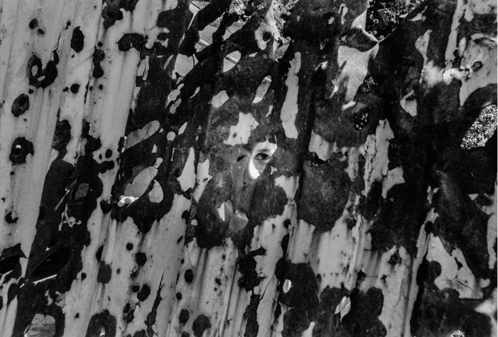 A child peers through the whole of a damaged piece of corrugated iron