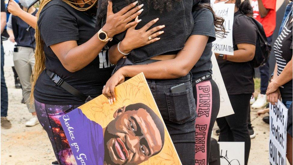 Women hugging while holding a George Floyd placard