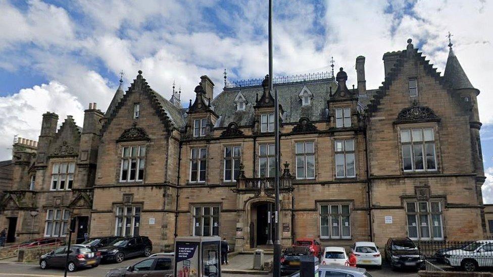 An old sandstone building with cars parked outside