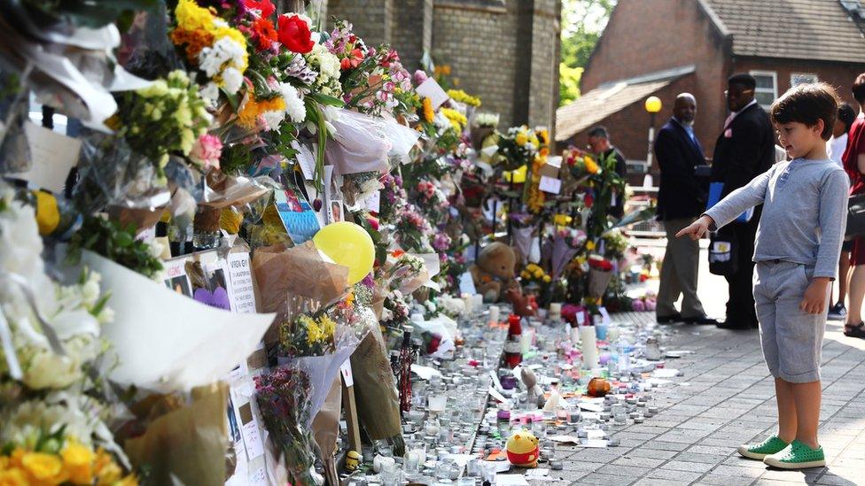 A boy points at flowers, tributes and messages left for the victims of the fire