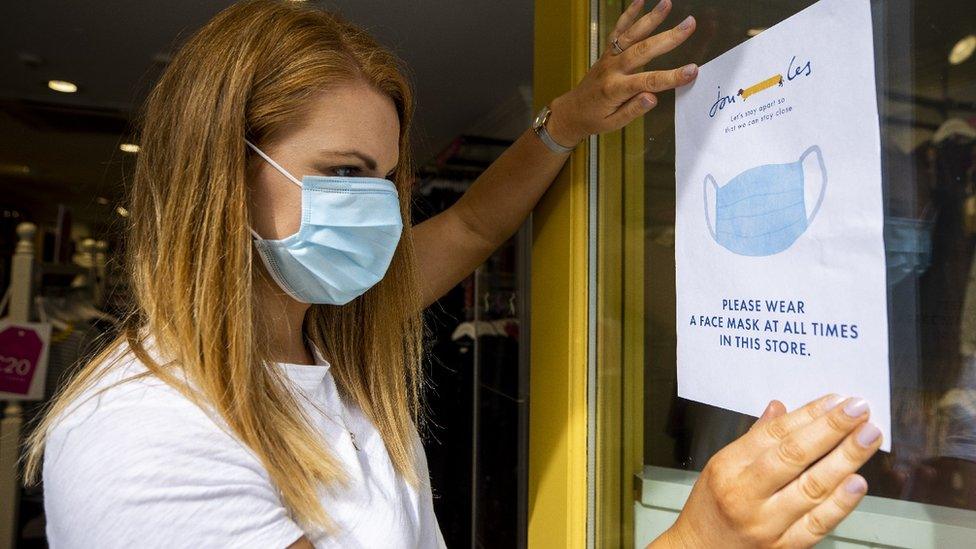 Shop owner holding up sign enforcing mask wearing in a shop