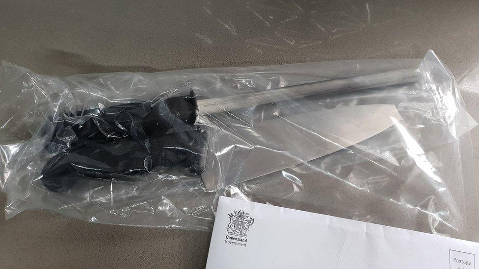 A knife and sharpener sealed within a plastic bag sit on top of a letter from Queensland Health