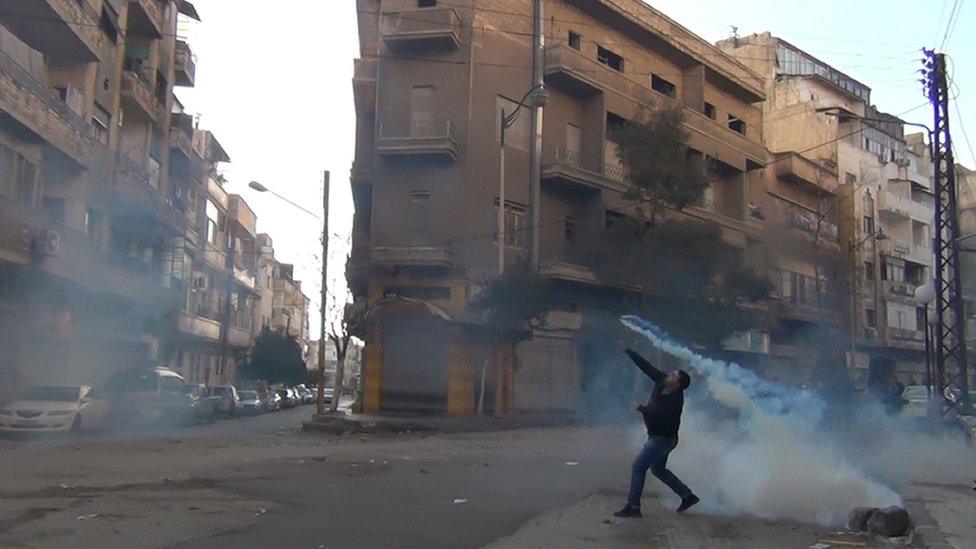 Protester throws tear gas at security forces at a demonstration in the city of Homs (December 2011)