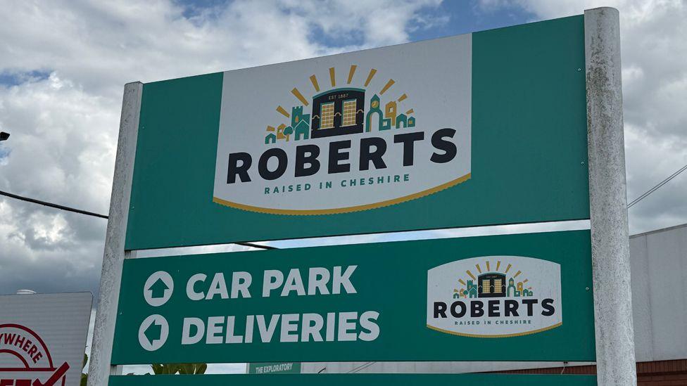 A turquoise-green sign with "Roberts: Raised in Cheshire" and car park and deliveries directions written on it
