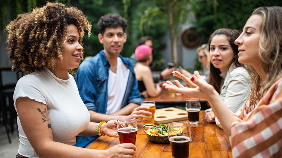 People talk outside with drinks and food