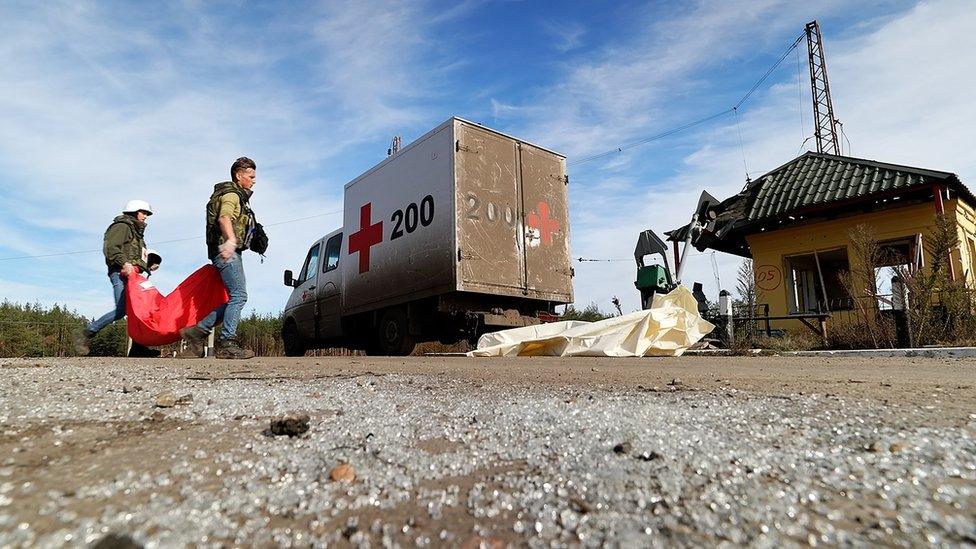 Artur and Denys carry a body bag to their van - marked with a red cross and the number 200.