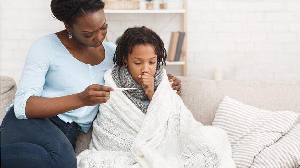 Child coughing and wrapped in a blanket and having their tempertature checked