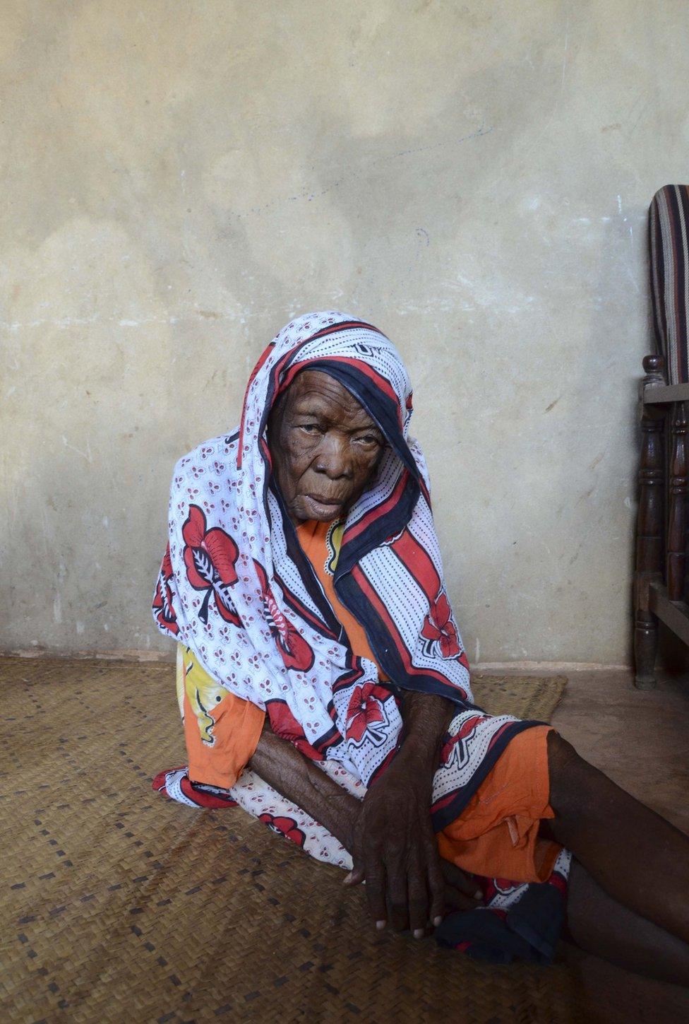 An elderly lady sits on the floor