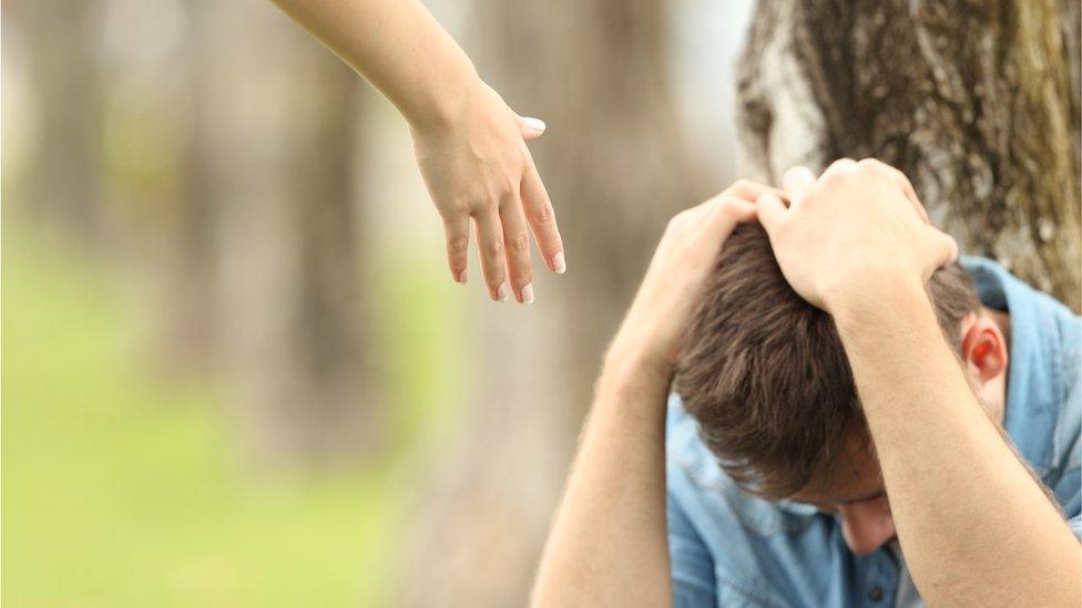 A hand reaches down to a teenager sitting with his head in his hands