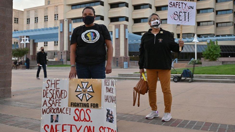 Two film workers hold signs calling for better safety on movie sets