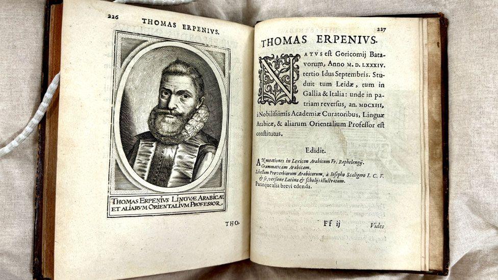 An open book showing on the left page a wood cut drawing of Thomas Erpenius, in an oval, wearing a ruff and with a full beard and on the right page words in Latin