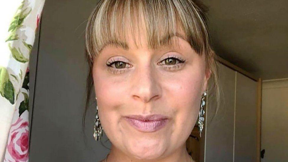 Sarah Albone: a woman with short light brown hair wearing long silver earrings.
