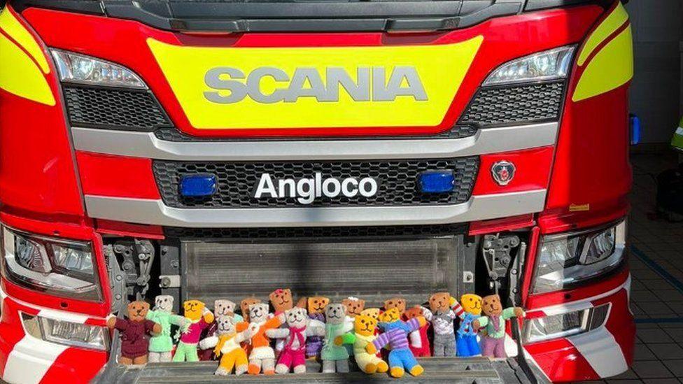 Two lines of colourful knitted teddies placed on the front of a fire engine