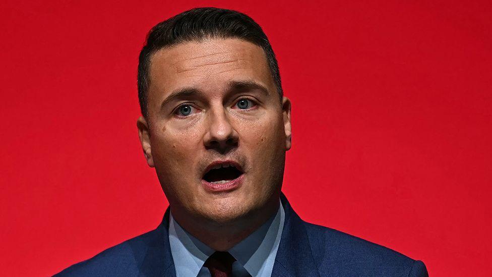 Head and shoulders crop against a red background of Wes Streeting looking away from camera as he speaks to a conference audience in Liverpool on 25 September