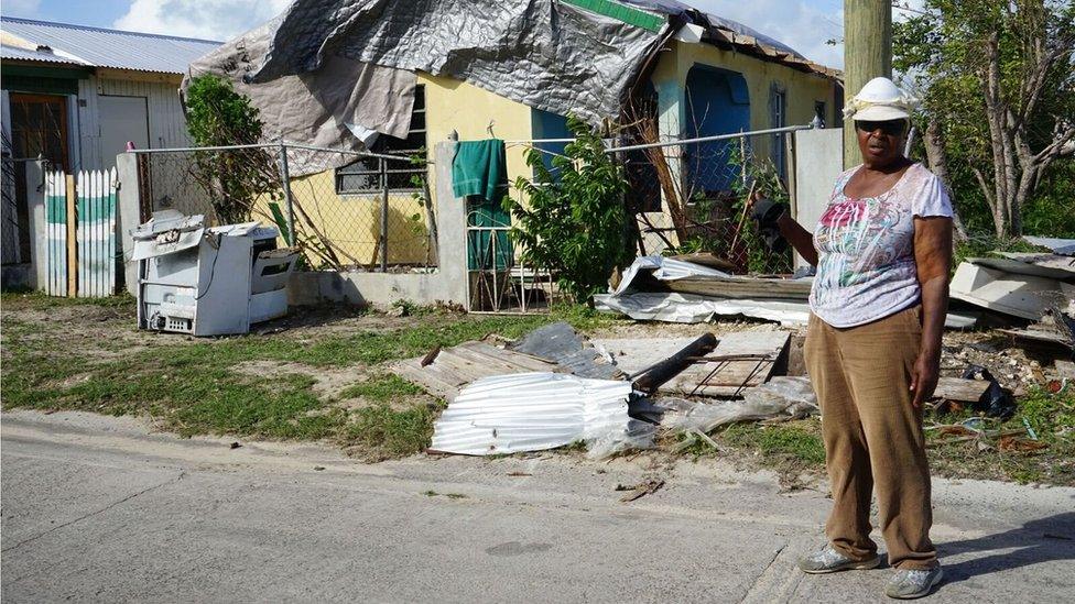 A Barbudan woman, Princess Harris-Parker, stands in front of a house covered in tarpaulin