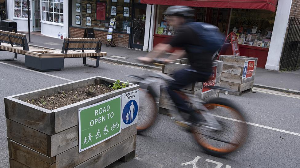 A blurred cyclist passes through the barriers that form an LTN (Low Traffic Neighbourhood), an experimental closure by Southwark Council preventing motorists from accessing the junction of Carlton Avenue and Dulwich Village