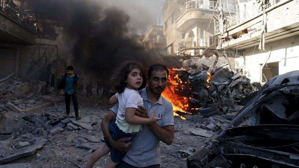 A man carries a girl as they run away from a site hit by what activists said were air strikes by forces loyal to Syria's President Bashar al-Assad in the Douma area of Damascus (24 August 2015)