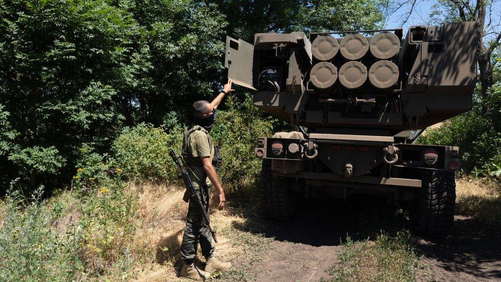 A Ukrainian soldier stands beside a HIMARS launcher