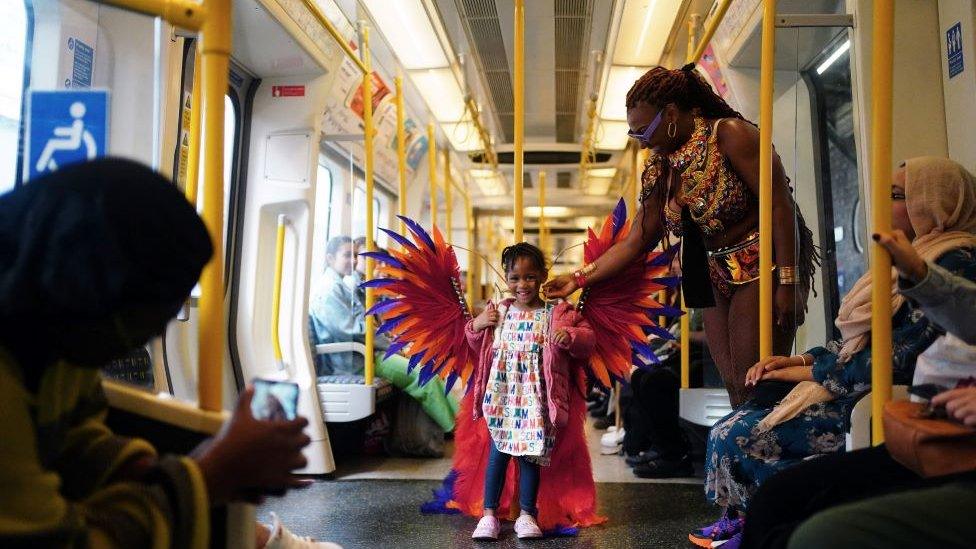 A young girl tries on a carnival goer's costume on the underground during the Notting Hill Carnival in London