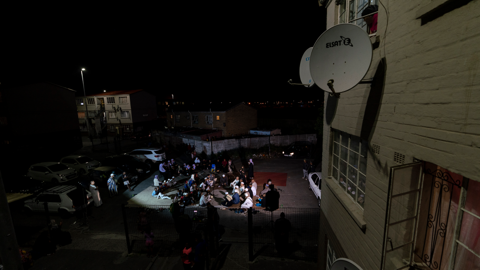 A woman looking down from a flat window at people gathered for dhikr in Manenberg, Cape Town - South Africa