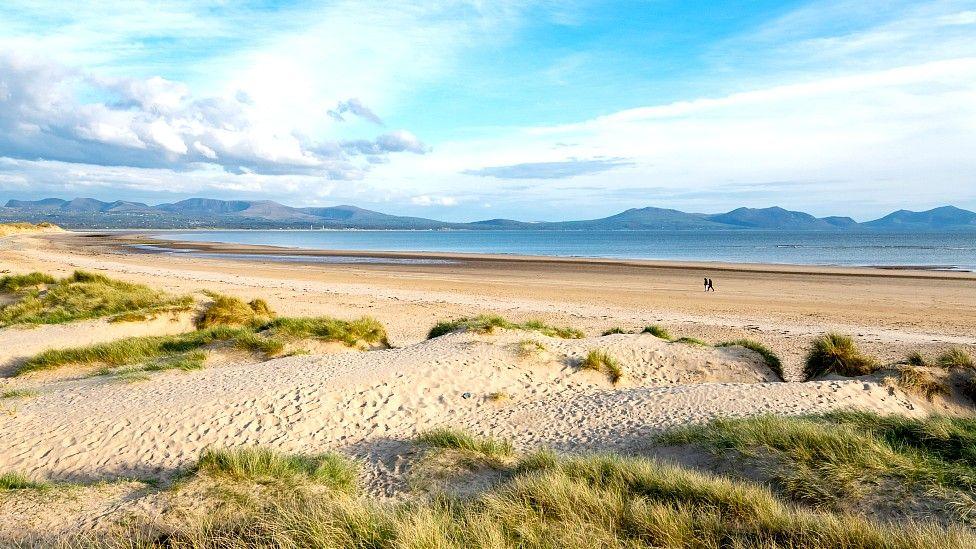 Wide shot of Llanddwyn beach with mountains in the background and two people in the distance