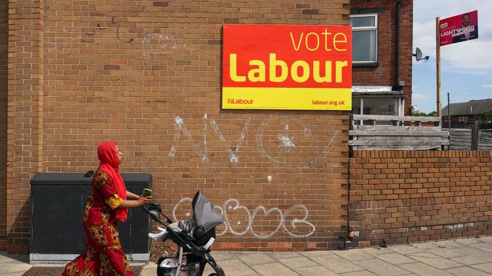 Woman passes campaign sign in Wakefield