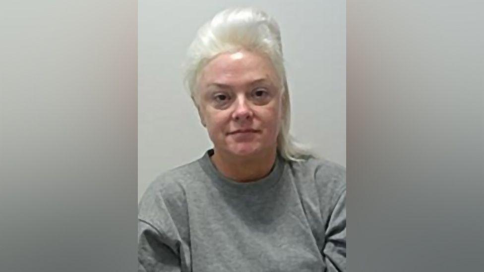 Catherine Hudson has no expression on her face in her mugshot. She is wearing a grey jumper and has her hair tied back.